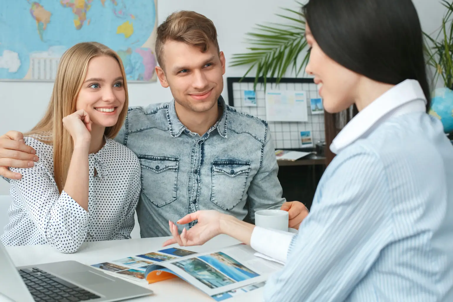 Young man and woman in a tour agency with a travel agent presenting destinations smiling