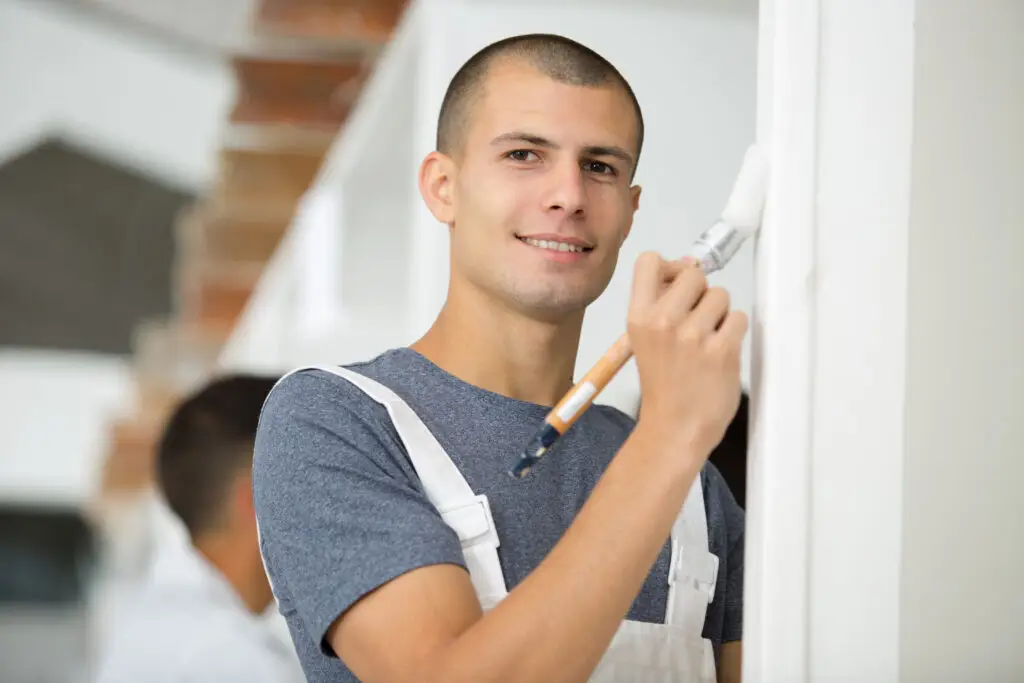 young man painter in uniform painting white wall