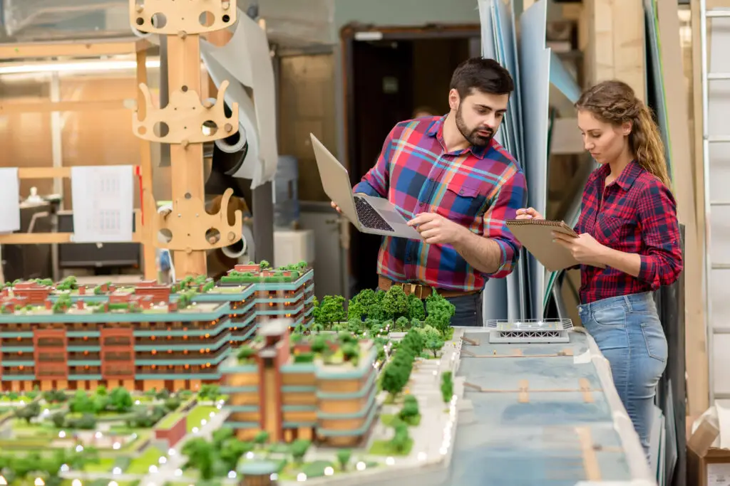 Two,Young,Architects,Reading,Working,Notes,In,Notepad,And,Searching