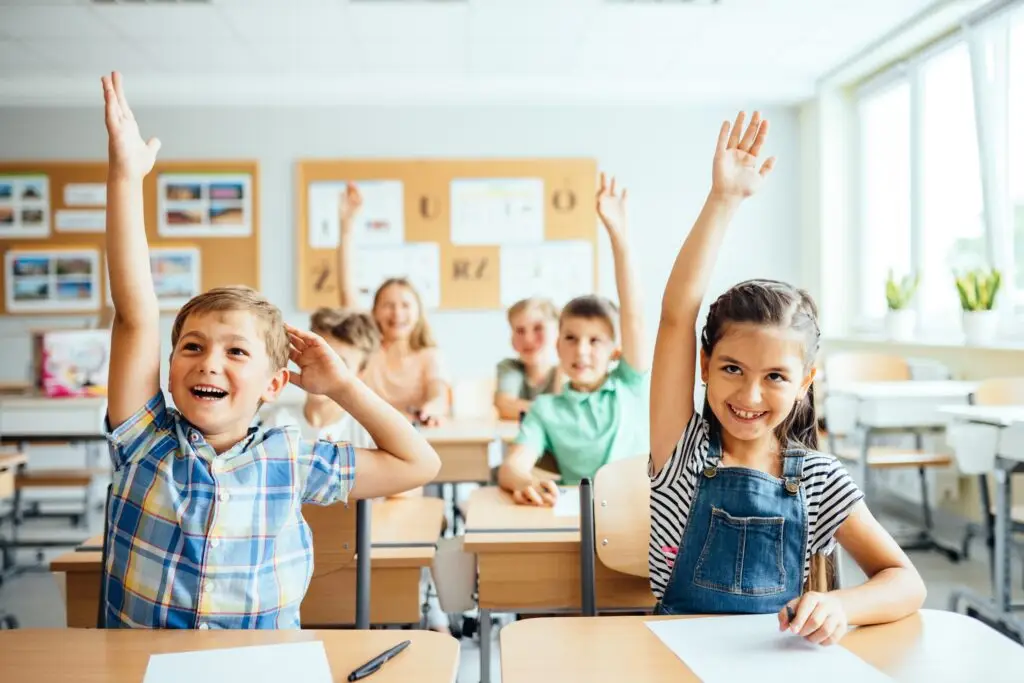 School,Children,In,Classroom,At,Lesson.,Little,Children,Raising,Hands