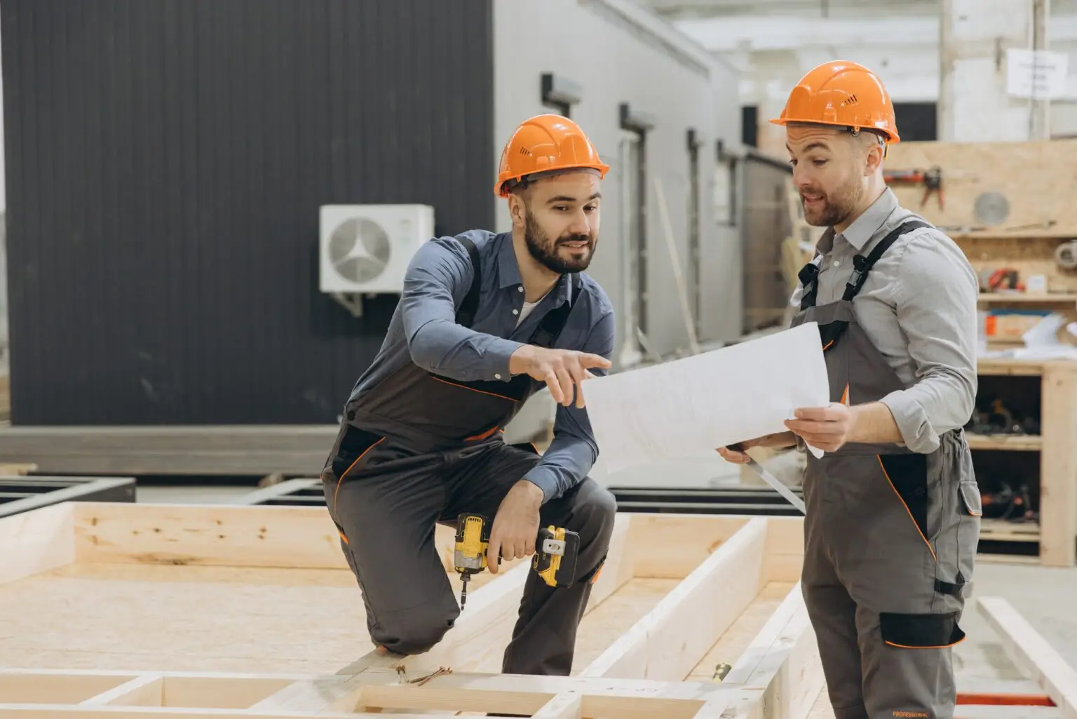 Two,Builders,In,Overalls,And,Hardhats,Are,Discussing,A,Blueprint